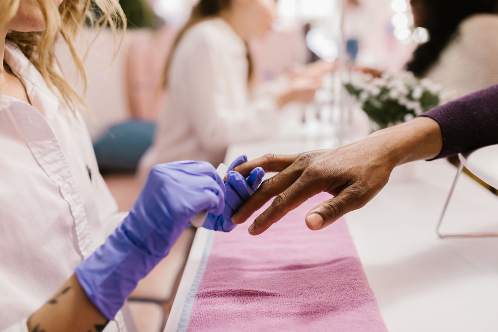 A nail technician in purple gloves doing a client’s manicure