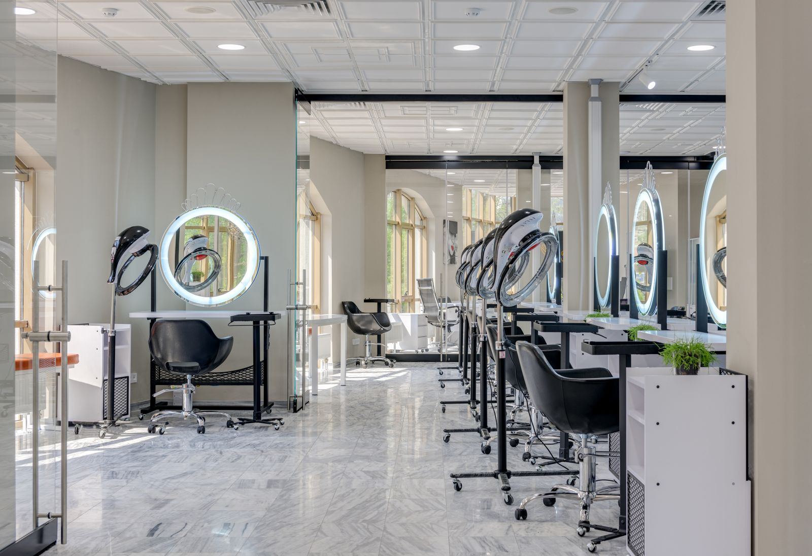 A long salon with a row of black chairs and round mirrors under bright ceiling lights
