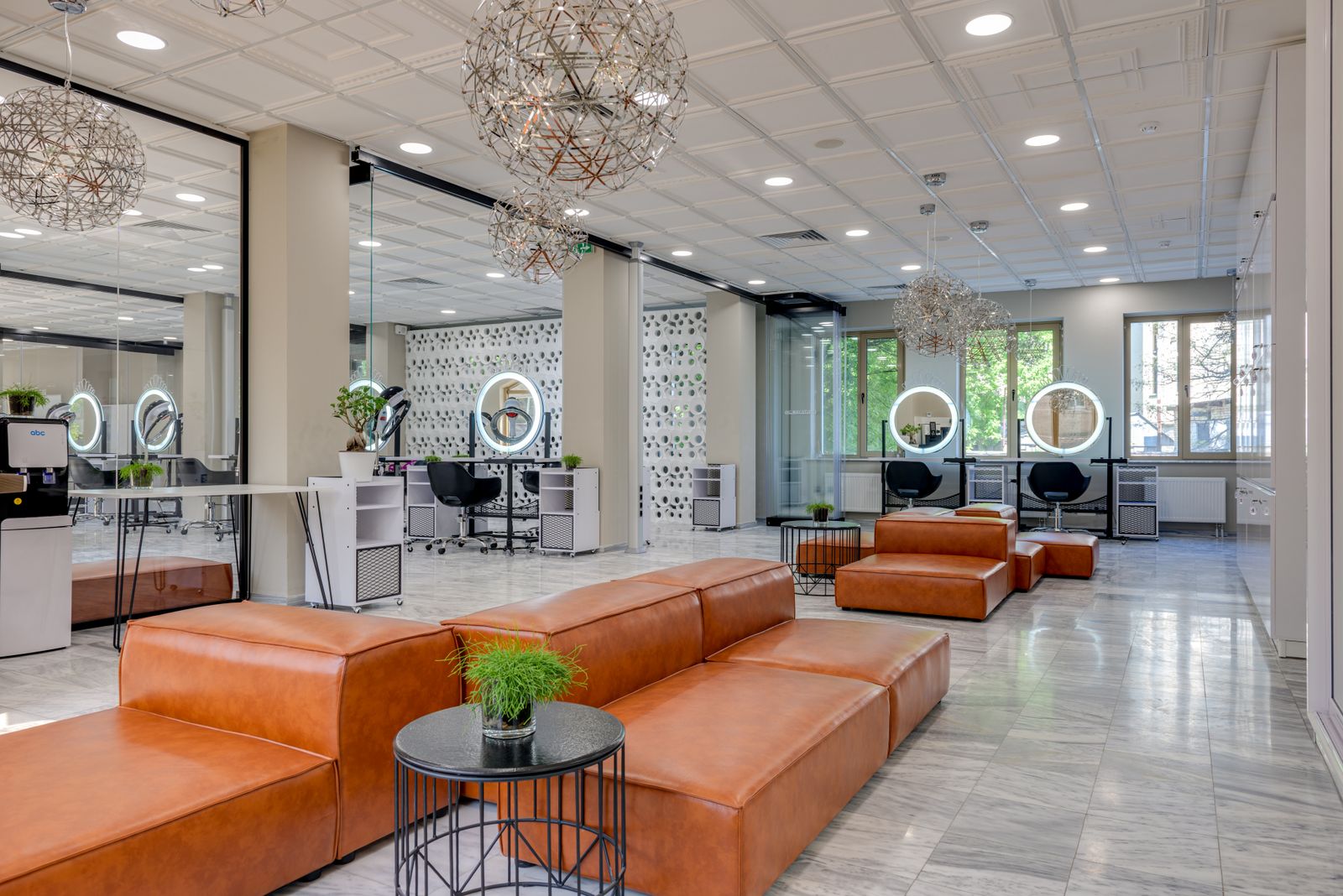 A bright salon with big round mirrors, black chairs and a tan leather lounge