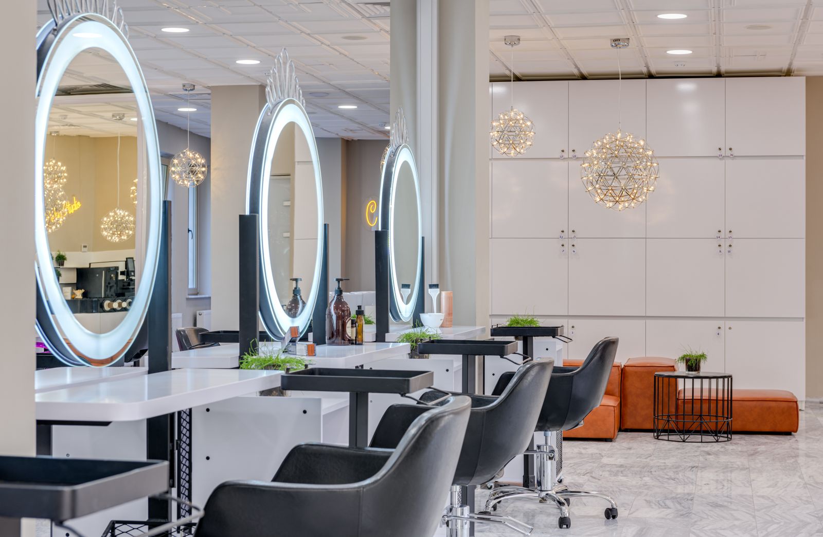 A bright salon with round lit mirrors, black styling chairs and marble floors